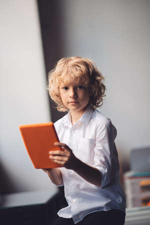 Serious boy. Cute blonde boy holding his tablet and looking serious