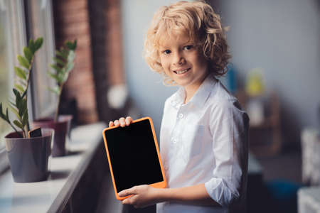 With tablet. Cute blonde boy showing his tablet and smiling