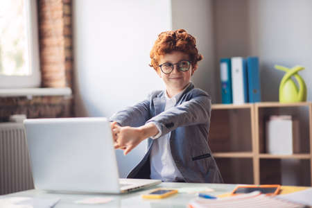 Tired. Red-haired boy in sitting at the laptop and stretching