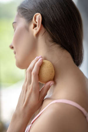 Relaxation. Pretty woman rubbing her neck with a sponge and looking relaxedの写真素材