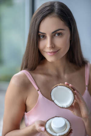 Face care. Woman in pink lingerie holding cream in her hands and smilingの写真素材