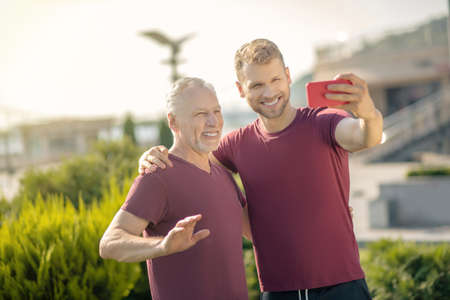Funny exercising. Young bearded male and mature grey-haired man making selfie during workout, smilingの写真素材