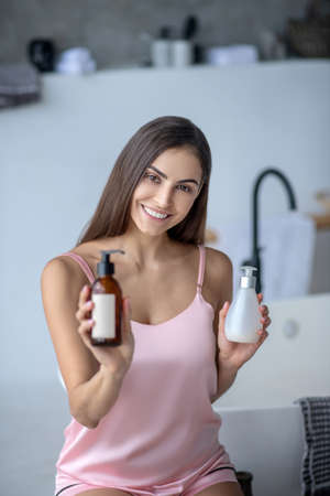 Choise of cosmetics. A woman holding two bottles of skincare productsの写真素材
