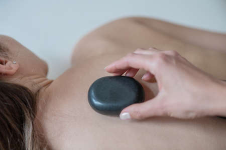 Stone therapy. Close up picture of a hand putting a stone on a womans back
