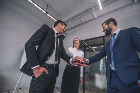Project preparation. Three colleagues standing, putting hands together, smilingの写真素材