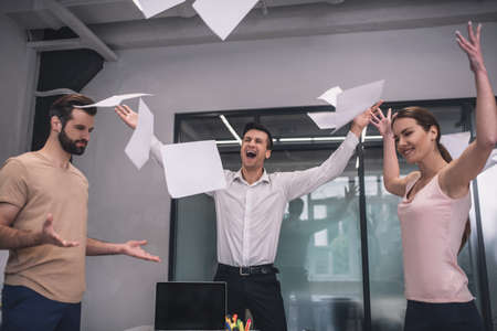 Good result. Happy female and two male coworkers tossing papers
