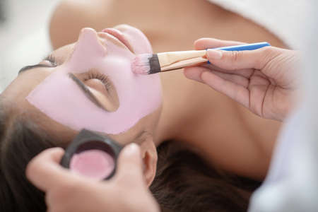 Beauty spa. Cosmetologist applying pink mask on womans faceのeditorial素材