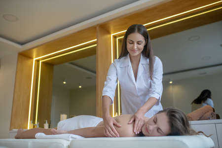 Back massage. Pretty massage therapist doing back massage to a female customer