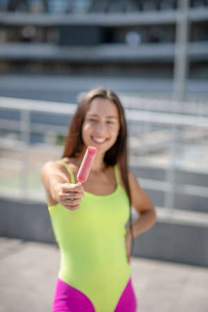Yummy. Girl in bright sportswear and roller-skates showing ice-cream