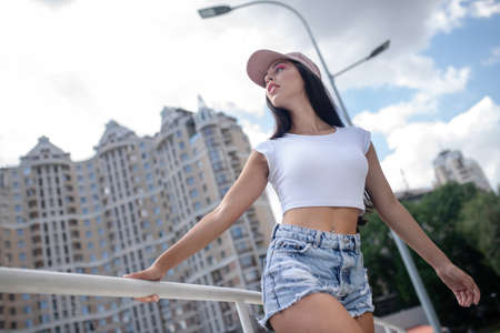 Looking good. Fit girl in jeans shorts and in cap looking asideの写真素材