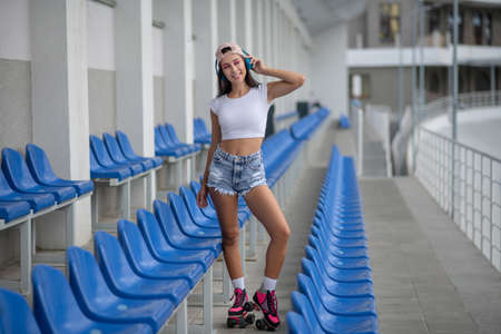 Sporty girl. Dark-haired girl in roller-skates listening to music and looking goodの写真素材