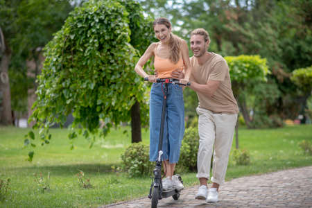 New experience. Young man helping his girlfriend to ride scooter