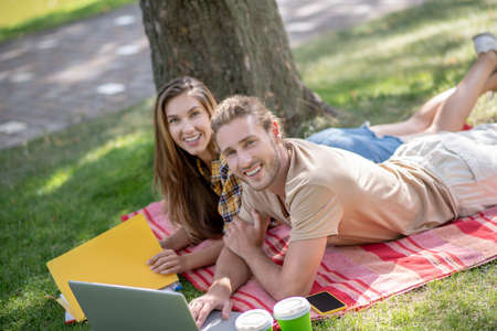 Studying on the park. Young happy couple lying on the grass and studying together