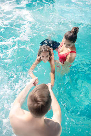 Swimming training. Young caring dad and mom in swimming suits teaching their son to swim, everyone in waterの写真素材