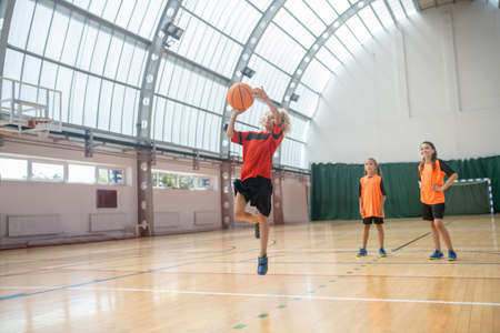 Jumping. Blonde boy in red tshirt jumping with a ball in hands