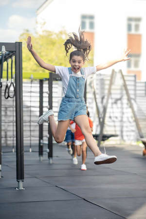 Playing. Cute girl in denim jumping while playing with friendsの写真素材
