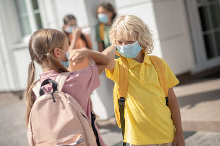 Greeting. Children in protective masks in the school yard greeting each otherの写真素材