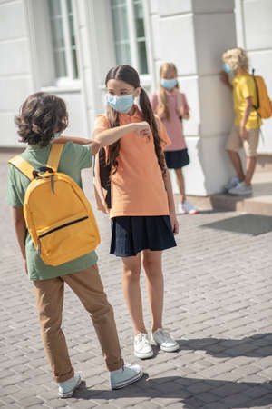 Friends. A boy and a girl in masks greeting each other in a school yardの写真素材