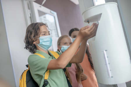 Disinfection. Boy in preventive mask getting some sanitizer into his handの写真素材