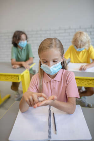 Disinfection. Fair-haired girl in a mask spraying sanitizer on her hands before lesson
