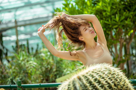 Feeling awesome. Pretty young woman standing near the cactus and holding her hairの写真素材