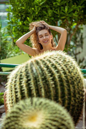 Greenhouse. Pretty young woman standing near the cactus and smiling happilyの写真素材