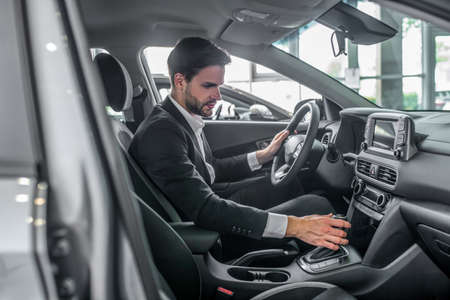 Test drive. Bearded young man in a black suit sitting in the new car
