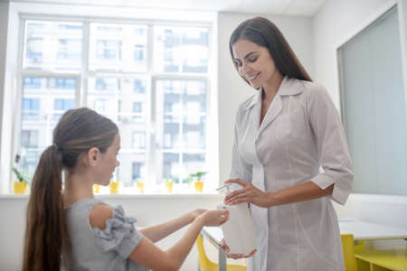 Hands disinfection. Doctor in a lab coat spraying sanitizer to girls handsの写真素材