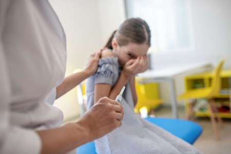 Vaccination. Girl in a blue dress sitting next to the doctor and feeling scared