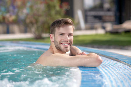 Happy man. Attractive smiling man in the water in an outdoor pool looking at the camera with his head turnedの写真素材