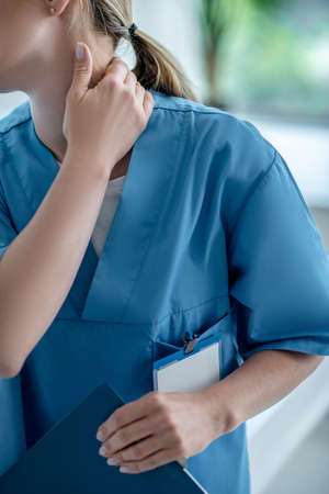 Painful. Close up of woman in blue lab coat touching her neck