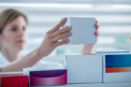 Drugstore. Close up of a pharmacist putting a medicine on the shelfの写真素材