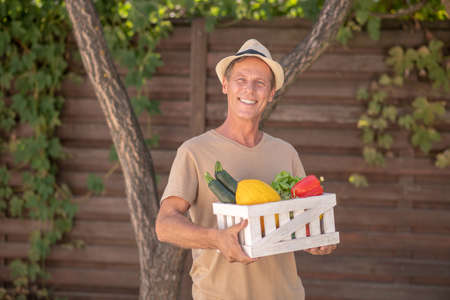 Harvest time. Smiling male in straw hat holding basket with vegetablesの写真素材
