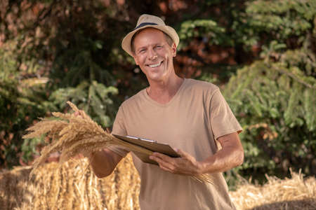 Harverst time. Male farmer holding clip folder and millet spikelets, smilingの写真素材