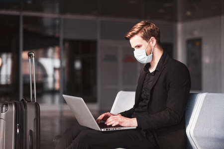 Waiting for the flight. A man wearing a face mask and using his computer in the airportの写真素材