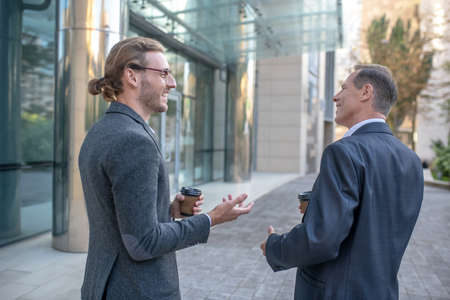 Coffee break. Two male business partners drinking coffee outside business center, discussing, smilingの写真素材