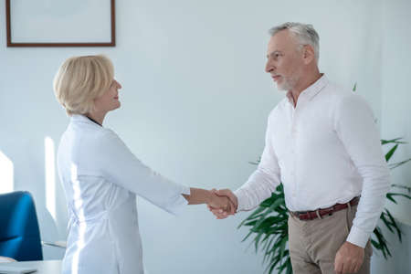 Medical advice. Gray-haired male patient shaking hands with blonde female doctorの写真素材