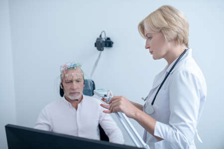 EEG examination. Serious female neurologist watching gray-haired male patient undergoing electroencephalogramの写真素材