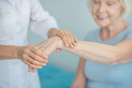 Wrist check up. Doctor examining wrist of an elderly smiling womanの写真素材