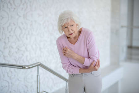 Aching elbow. Elderly woman in a pink shirt suffering from pain in elbowの写真素材