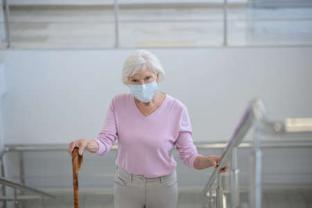 Upstairs. Grey-haired woman in facial mask going upstairsの写真素材