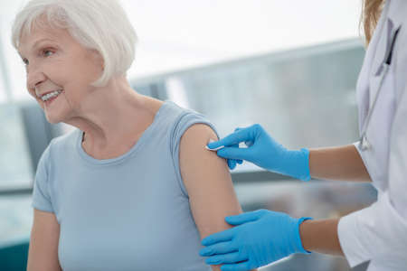 Injection. Nurse making an injection to an elderly smiling woman