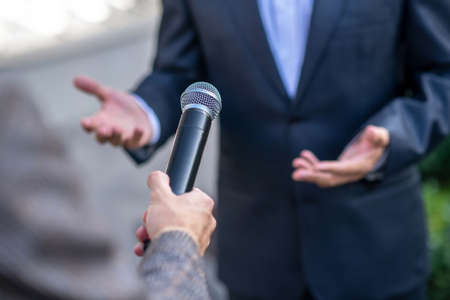 Journalistic interview. Close-up of male hands holding microphone during interviewの写真素材