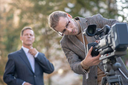 Journalistic interview. Fair-haired male journalist fitting camera to tripod before interview