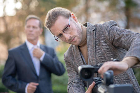 Journalistic interview. Fair-haired male journalist fitting camera to tripod, getting ready for...