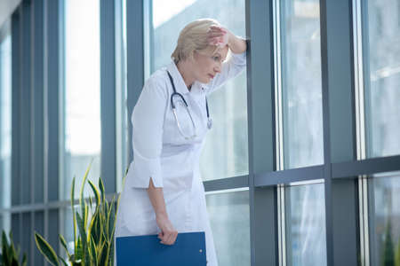 Medical profession. Tired female doctor leaning her forehead on the windowの写真素材