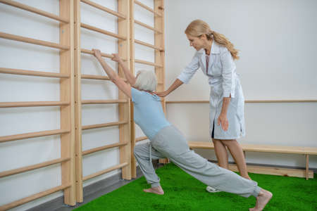 Exercising. Elderly woman doing lunging near a wall-mounted ladder with instructorの写真素材