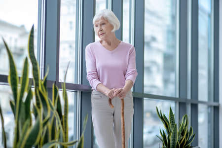 Alone. Elderly woman with a walking stick standing and looking thoughtfulの写真素材