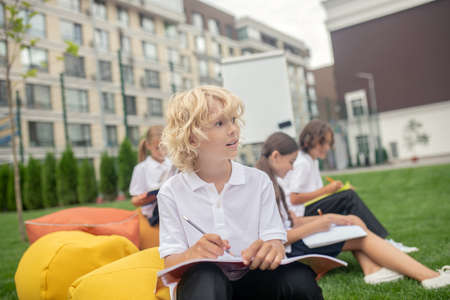 Thinking. Blonde boy in white shirt looking thoughtful at the lessonの写真素材