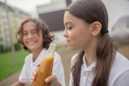 Lunch time. Long-haired girl drinking juice and smiling to her friendの写真素材